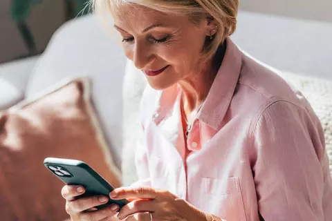 Frau sitzt auf der Couch und schaut auf das Handy